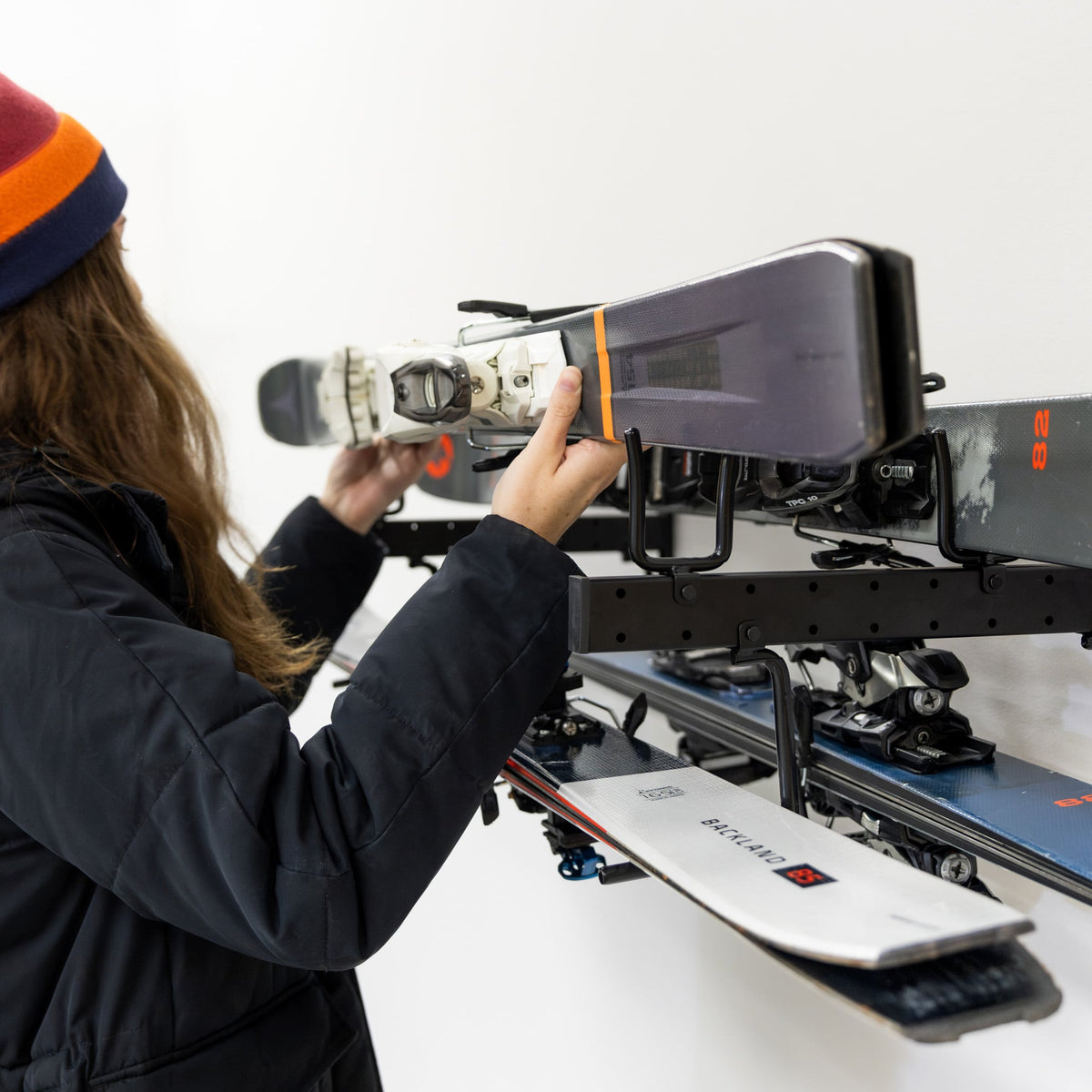 Woman placing a snowboard on the Cascade wall organizer above skis