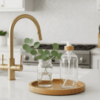 Clear glass soap bottle on a wooden tray beside a brass faucet