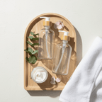 Two clear glass pump bottles on a wooden tray with a towel