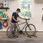 Man rolling a bike into the floor stand in a garage