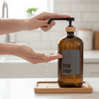 Hand pumping dish soap from the amber bottle on a wooden tray