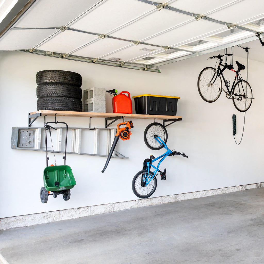 Garage wall with a long bracket shelf holding tires and bins, with bikes and a wheelbarrow hung below