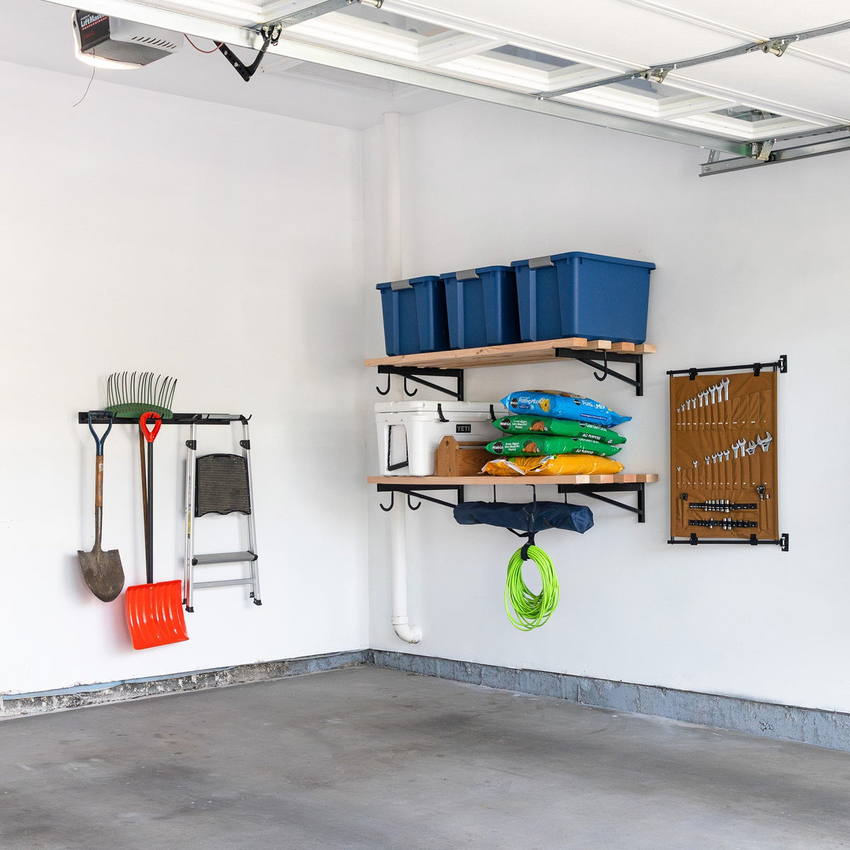 Garage wall with DIY bracket shelves holding blue bins beside hanging yard tools