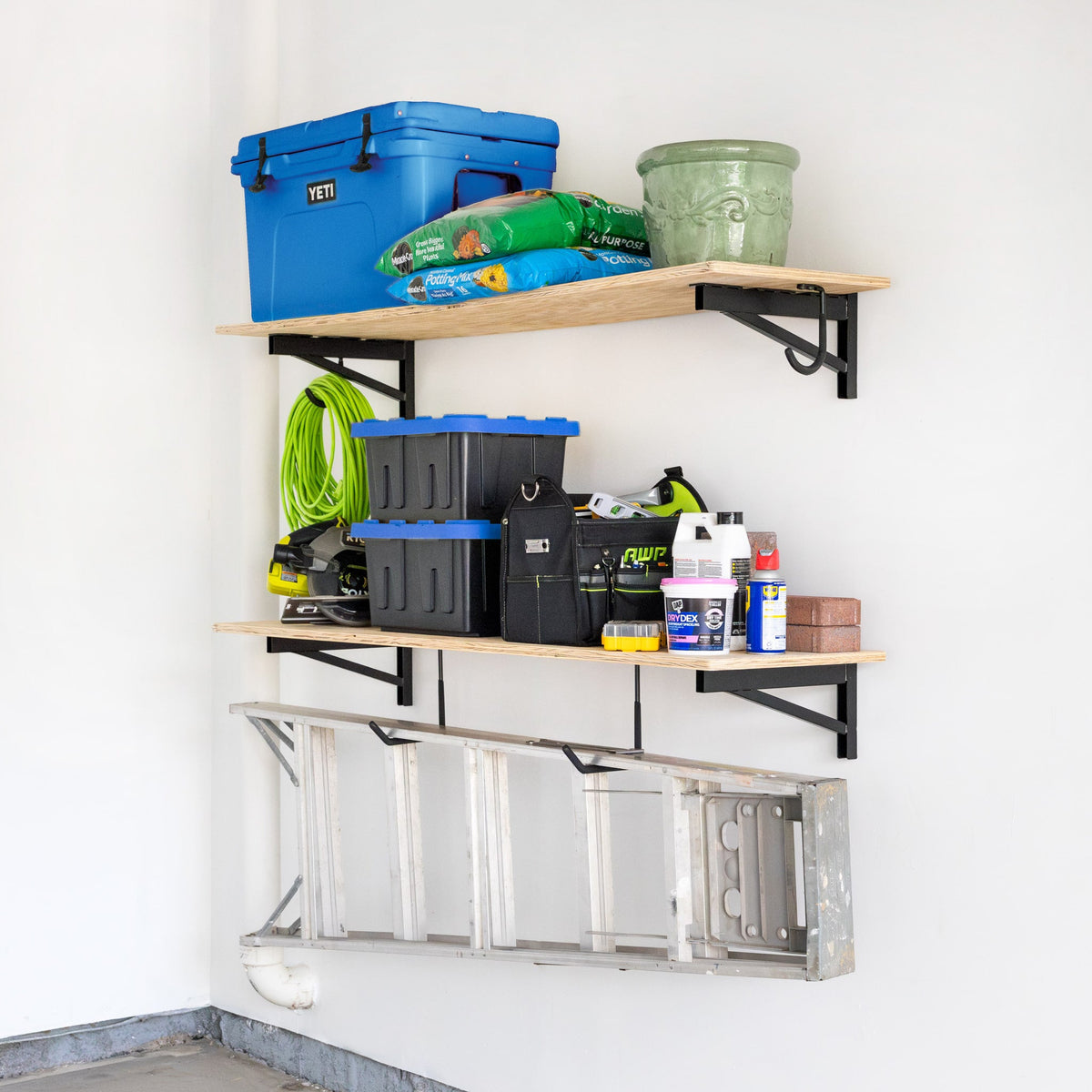DIY brackets holding two wood shelves with bins and supplies, with a ladder hung below
