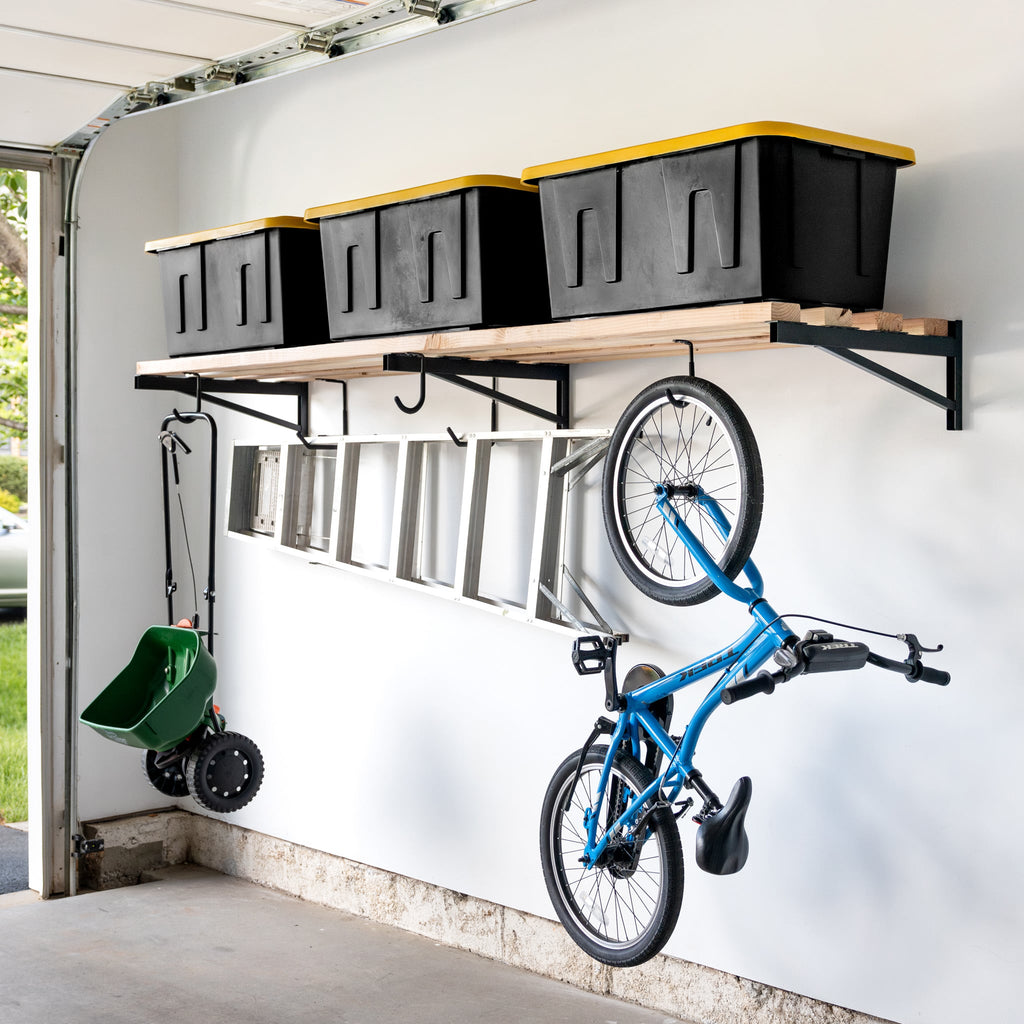 Long 2 x 8 ft wood shelf on three DIY brackets holding totes, with a bike and ladder hung below