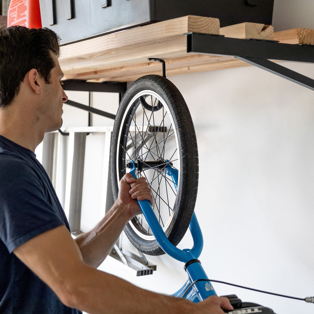 Man hanging a kids bike on a hook under the bracket shelf