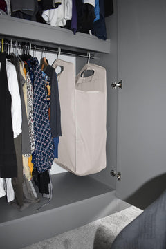 Beige laundry hamper hanging from a clothes rail inside a closet