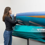 Woman sliding a kayak onto the mud-colored rolling rack