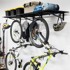 Two bikes hanging from hooks under a black wall shelf holding bins and a helmet