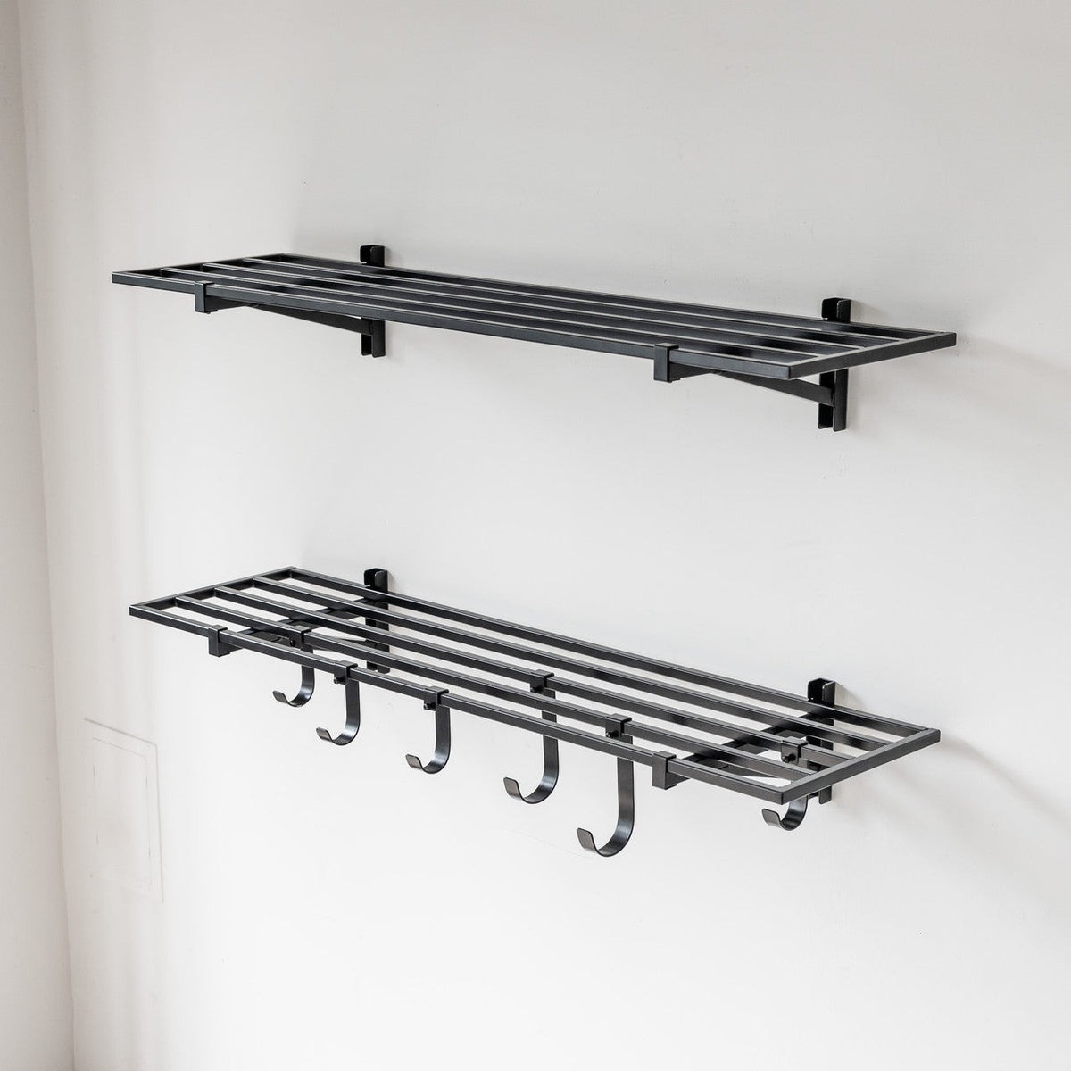 Two empty black 1 x 4 ft wall shelves, the lower one with hooks