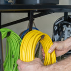 Hand hanging extension cords from hooks under a black wall shelf