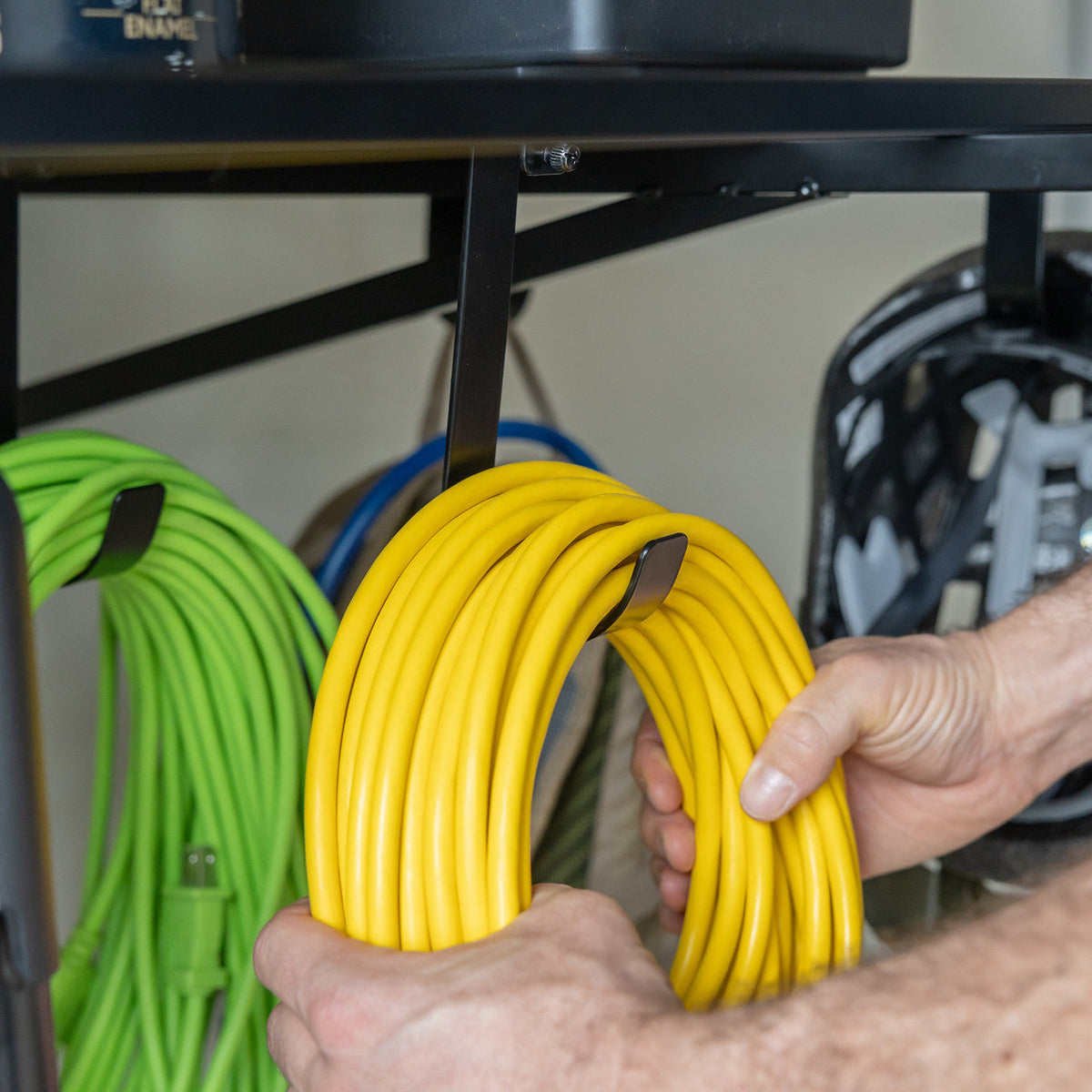 Hand hanging extension cords from hooks under a black wall shelf