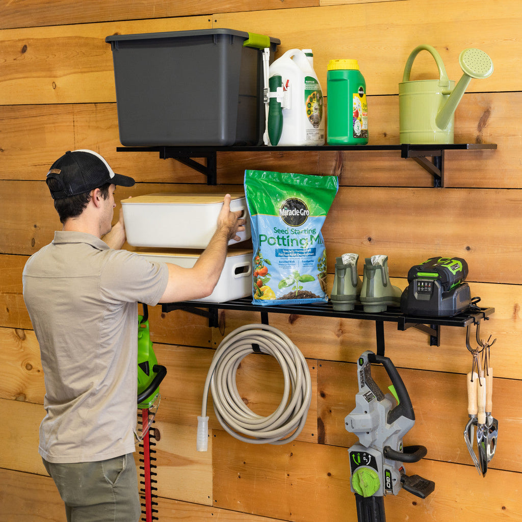 Man placing potting mix on black wall shelves on a wood wall with a hose hung below
