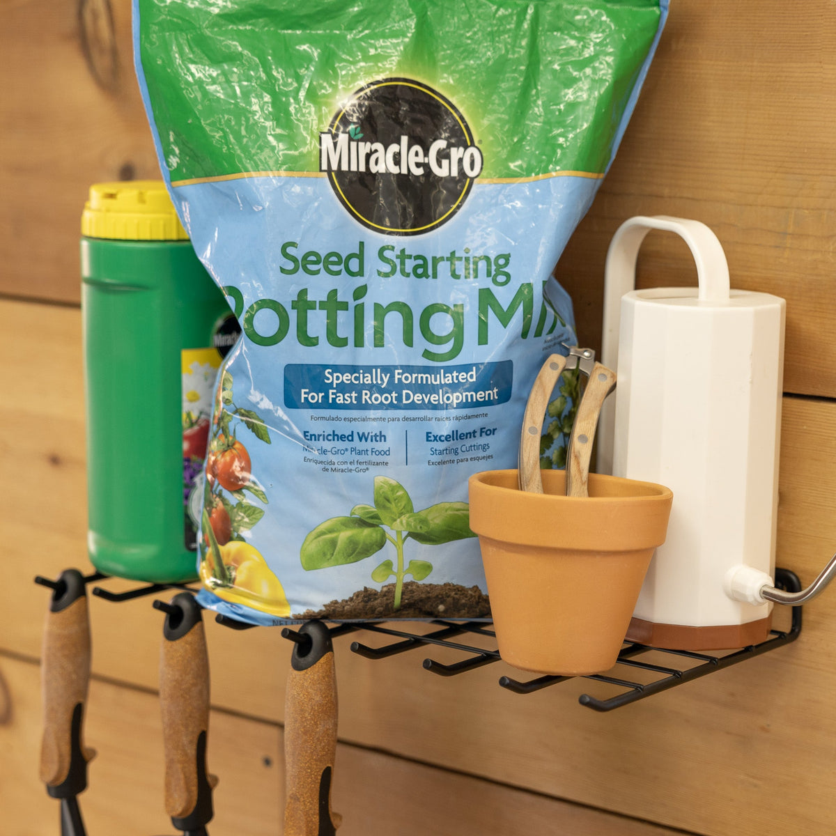 Garden tool shelf holding potting mix, a pot and watering can with tools hung underneath