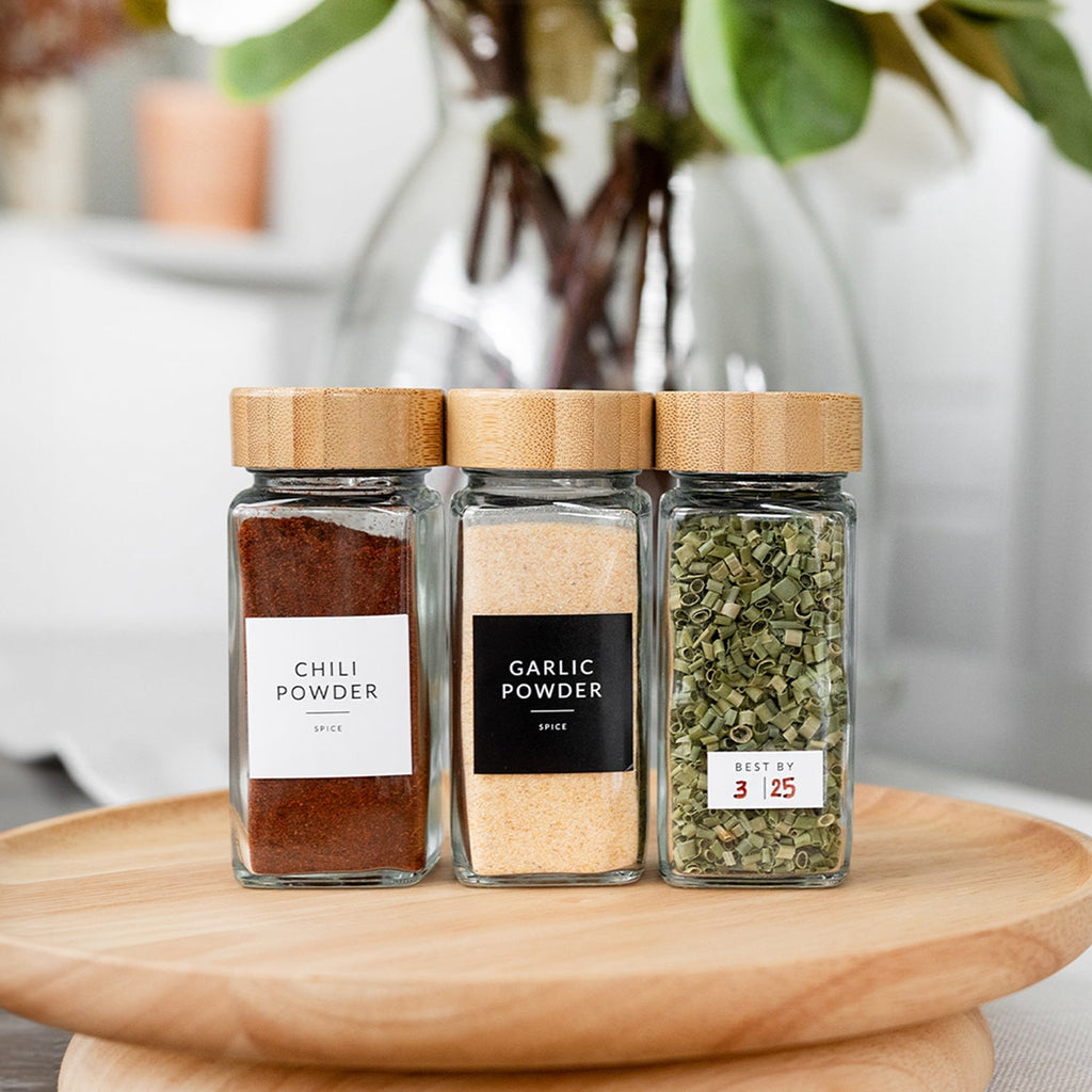 Three labeled square glass spice jars with bamboo lids on a wooden turntable