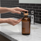 Hand pressing the pump of the amber hand soap bottle at a bathroom sink