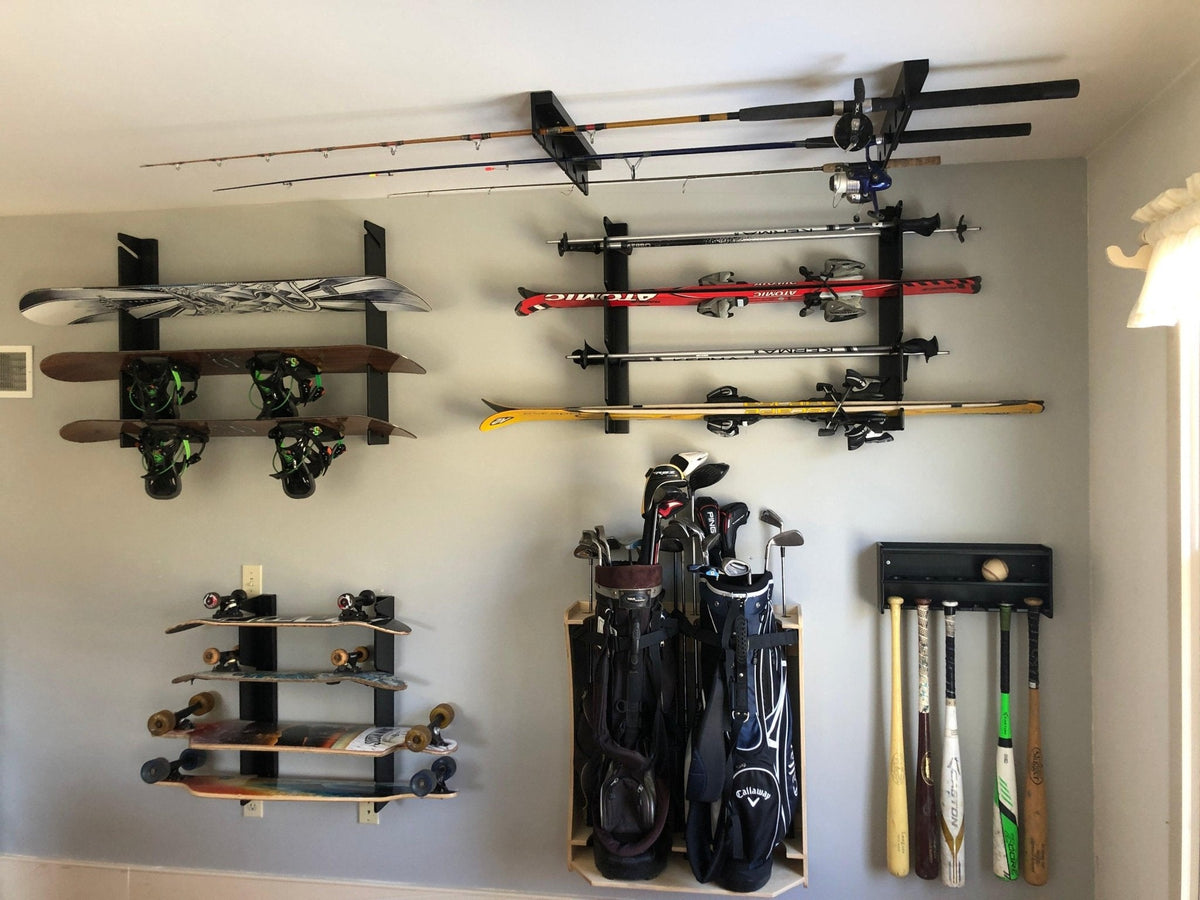 Snowboard and fishing rod racks mounted on a wall beside golf bags