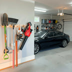 Hook rack holding yard tools and a leaf blower on a garage wall beside a car
