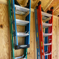 Three stepladders stored upright on a shed wall ladder rack