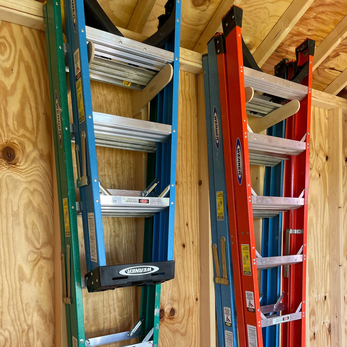 Three stepladders stored upright on a shed wall ladder rack