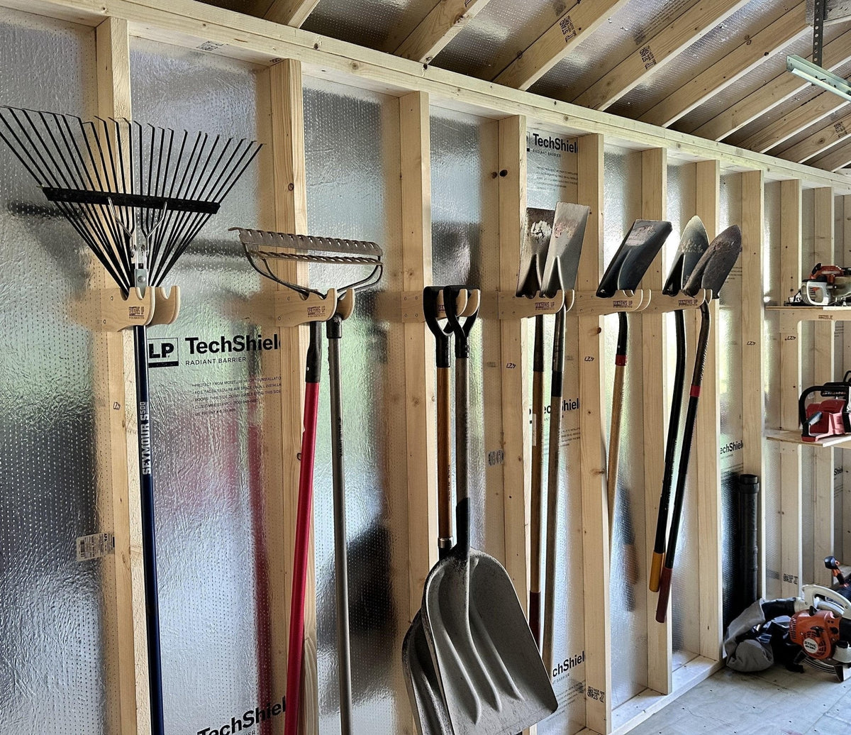 Rakes and shovels hanging on garden tool hooks along a shed wall