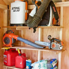Shed shelves holding a backpack blower, chainsaw and gas cans