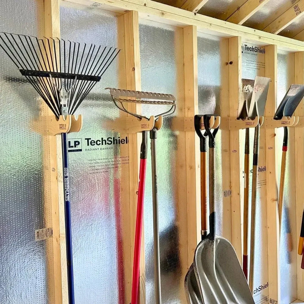 Rakes and shovels hanging on wood racks along a shed wall