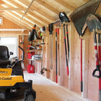 Shed with yard tools on wall racks beside a riding mower