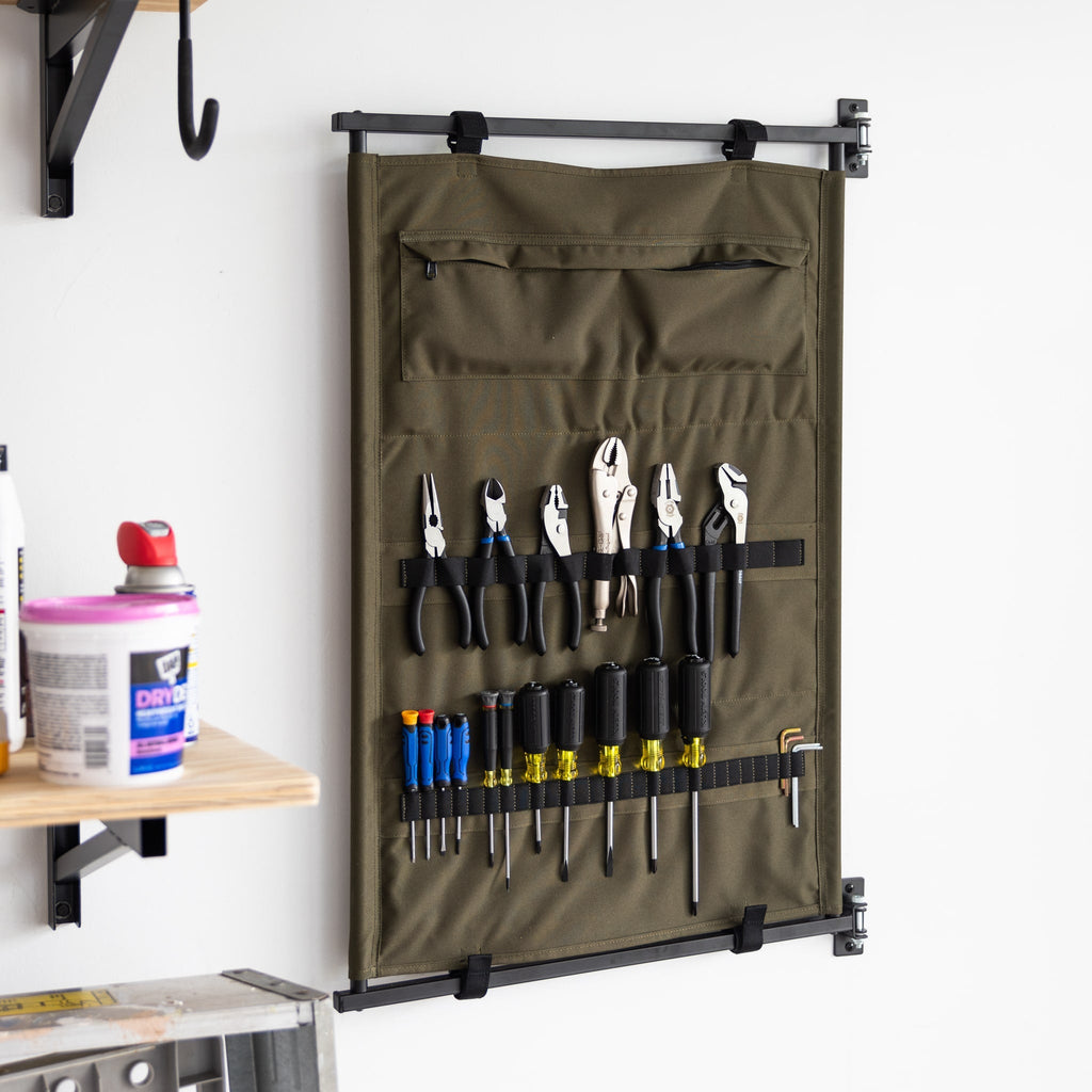Green canvas Pivot Panel holding pliers and screwdrivers beside a wall shelf