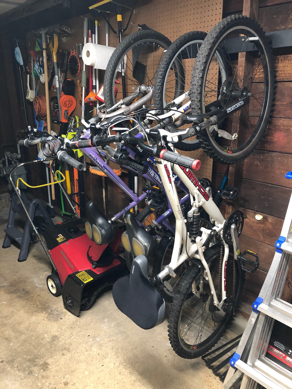 Garage wall with bikes hanging on the rack above a lawn mower