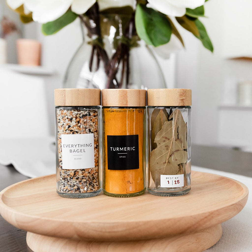 Three labeled round glass spice jars with bamboo lids on a wooden turntable