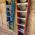 Two stepladders stored upright on a shed wall rack