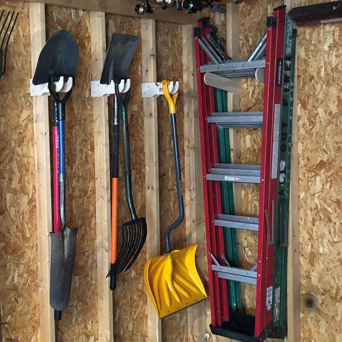 Step ladders stored on a wall rack beside shovels and a snow shovel