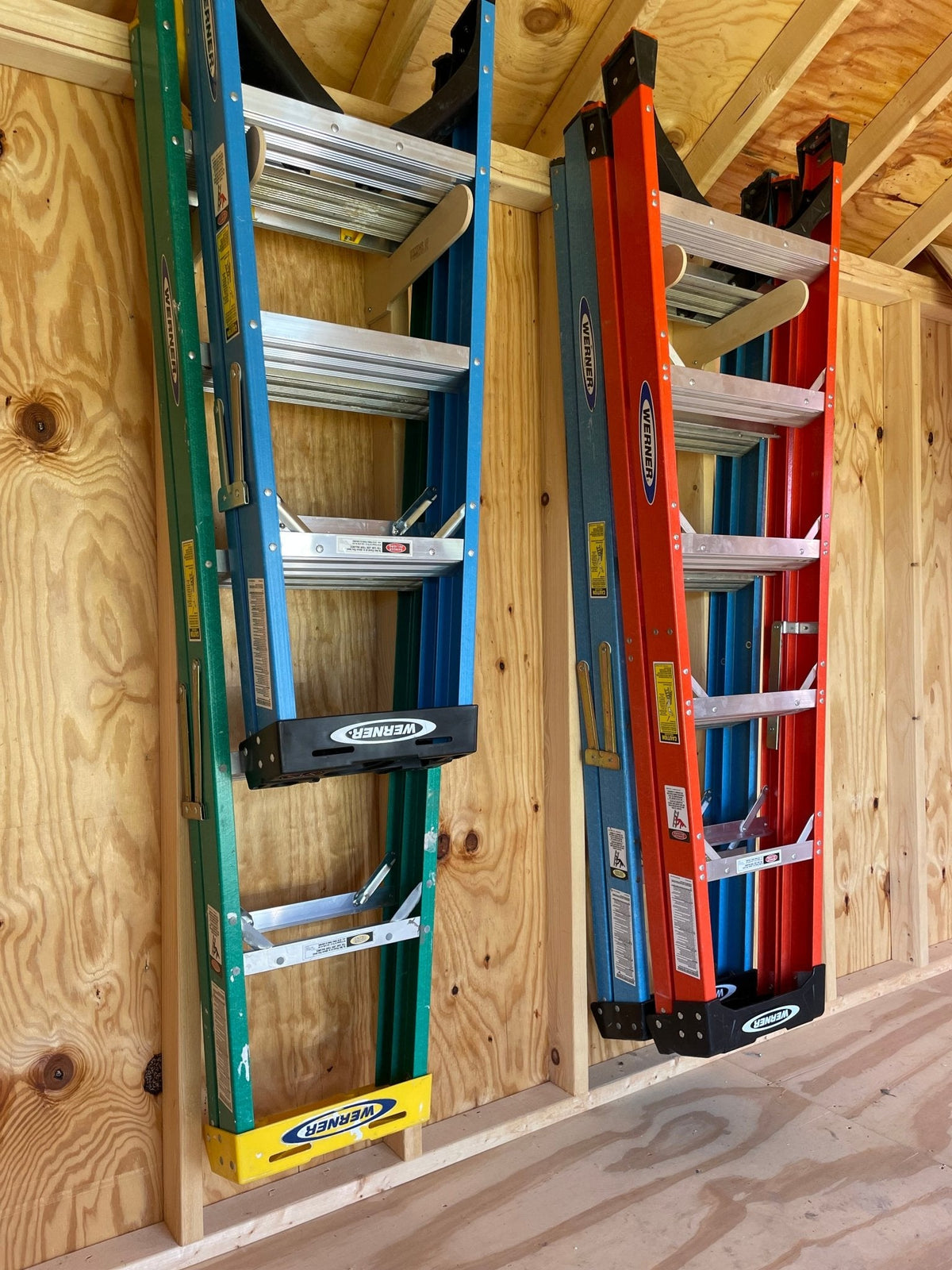Two stepladders stored upright on a shed wall rack