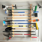 Wall-mounted garden tool rack holding rakes, shovels and a trimmer in a garage