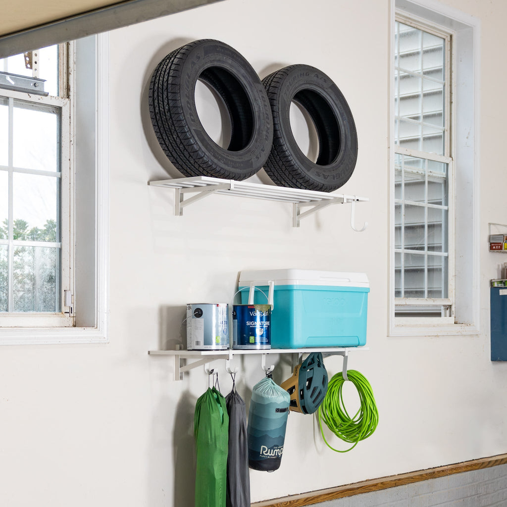 White wall shelves holding tires and a cooler, with bags and a hose hung below