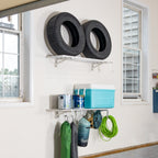 White wall shelves holding tires and a cooler, with bags and a hose hung below