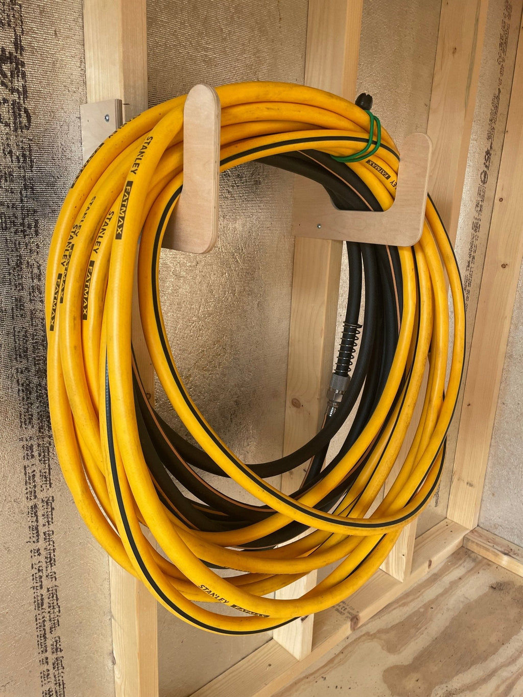 Hose coiled on a wood hose hook on a shed wall