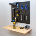 Folding wood workbench below a pegboard holding hand tools and a drill